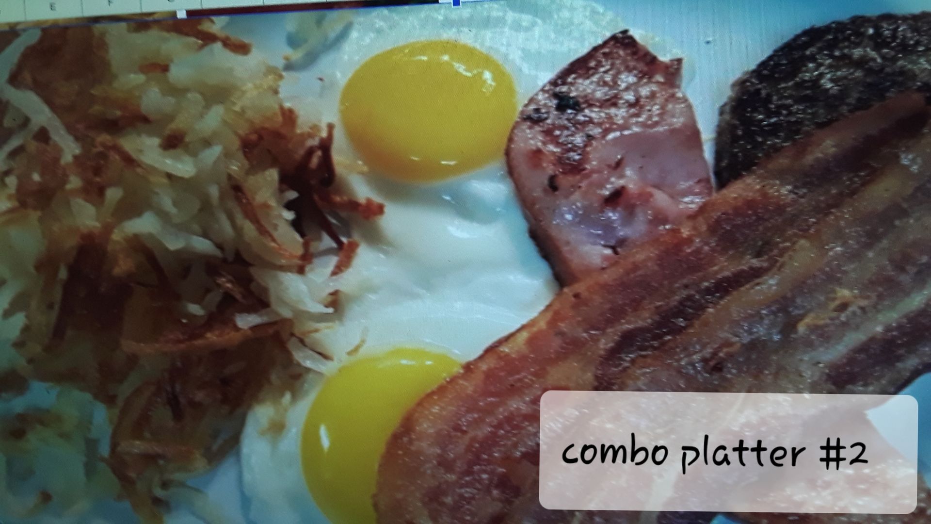 A breakfast combo platter featuring two fried eggs, crispy hash browns, a slice of ham, and strips of bacon.