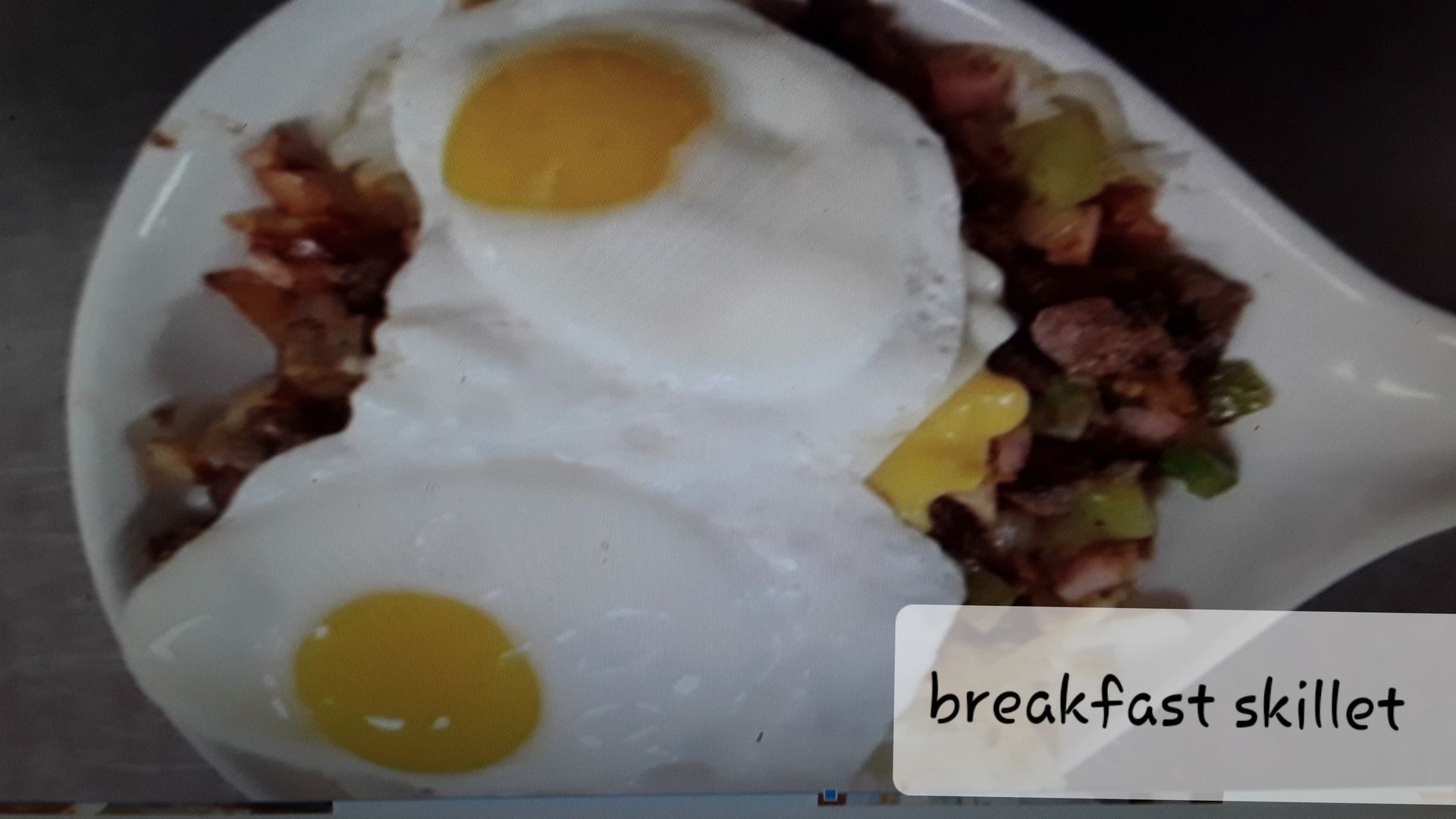 A breakfast skillet topped with two sunny-side-up eggs served in a white dish.
