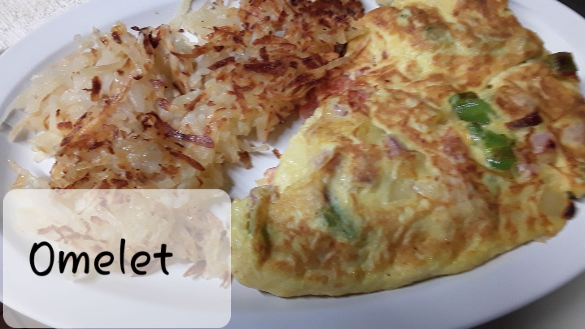 A golden-brown omelet filled with diced vegetables served on a white plate with a side of crispy shredded hash browns.