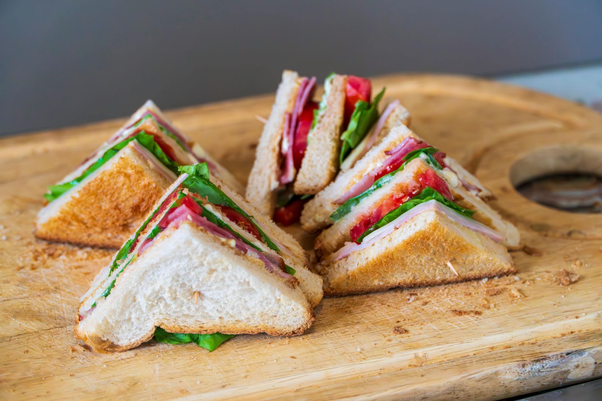 Four toasted club sandwich triangles arranged on a wooden cutting board against a gray background.