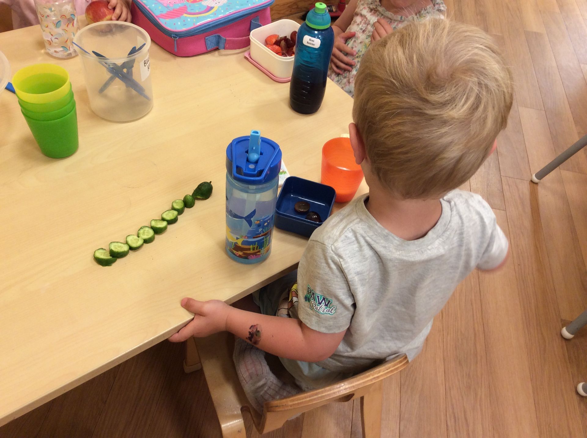 A young boy is sitting at a table with cucumber slices on it.