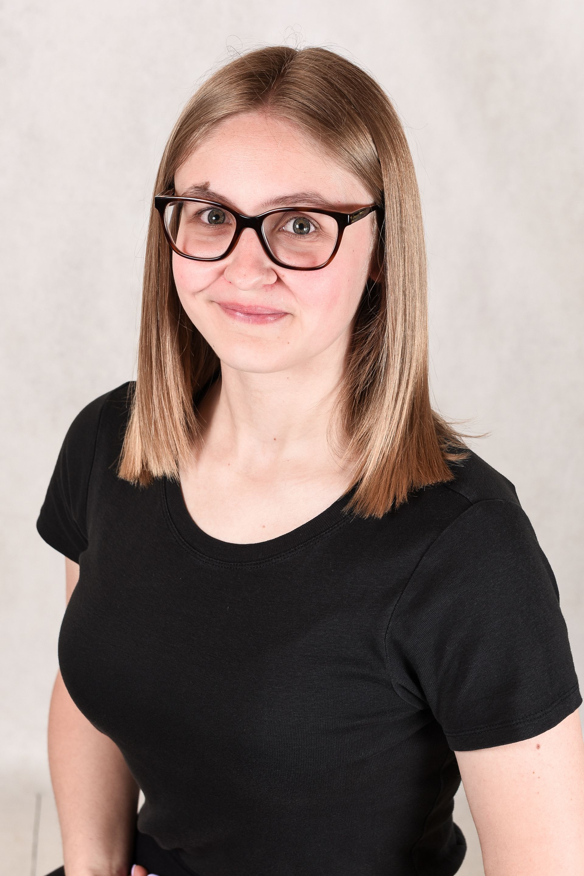 A young woman wearing glasses and a name tag is smiling for the camera.