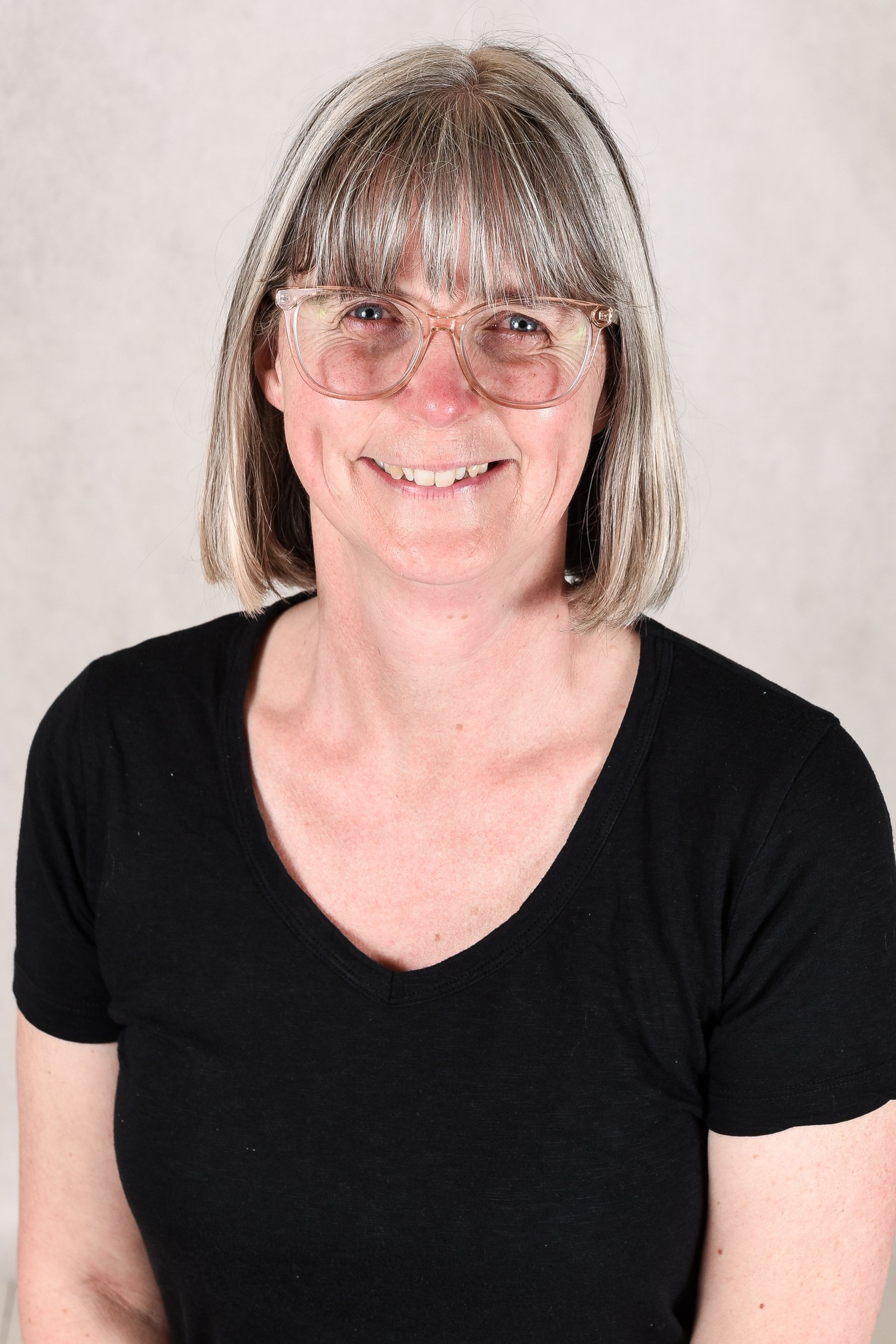A woman wearing glasses and a name tag is smiling for the camera.