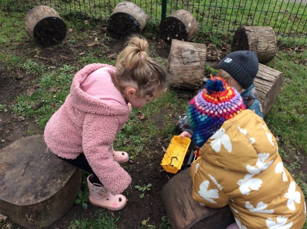 A girl and a boy are playing in the dirt with a toy truck.