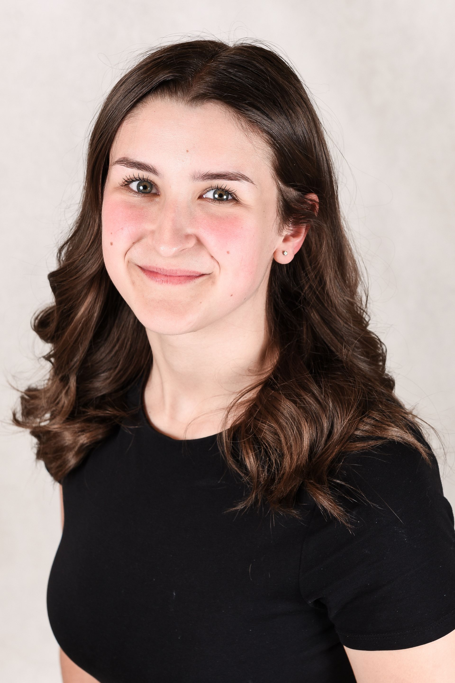 A young woman wearing a black shirt and a yellow name tag is smiling for the camera.