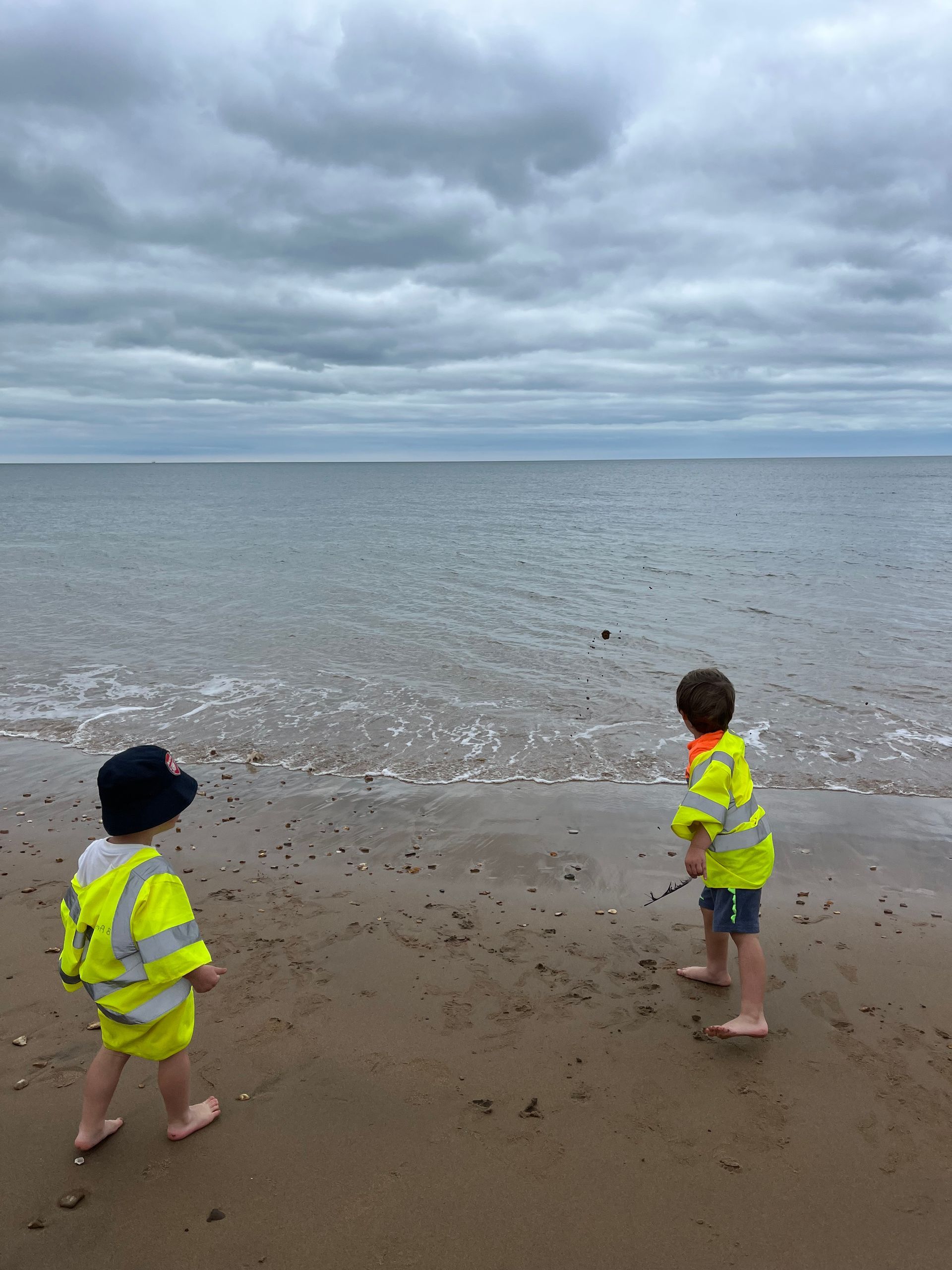 Two children are standing on a beach looking at the ocean.