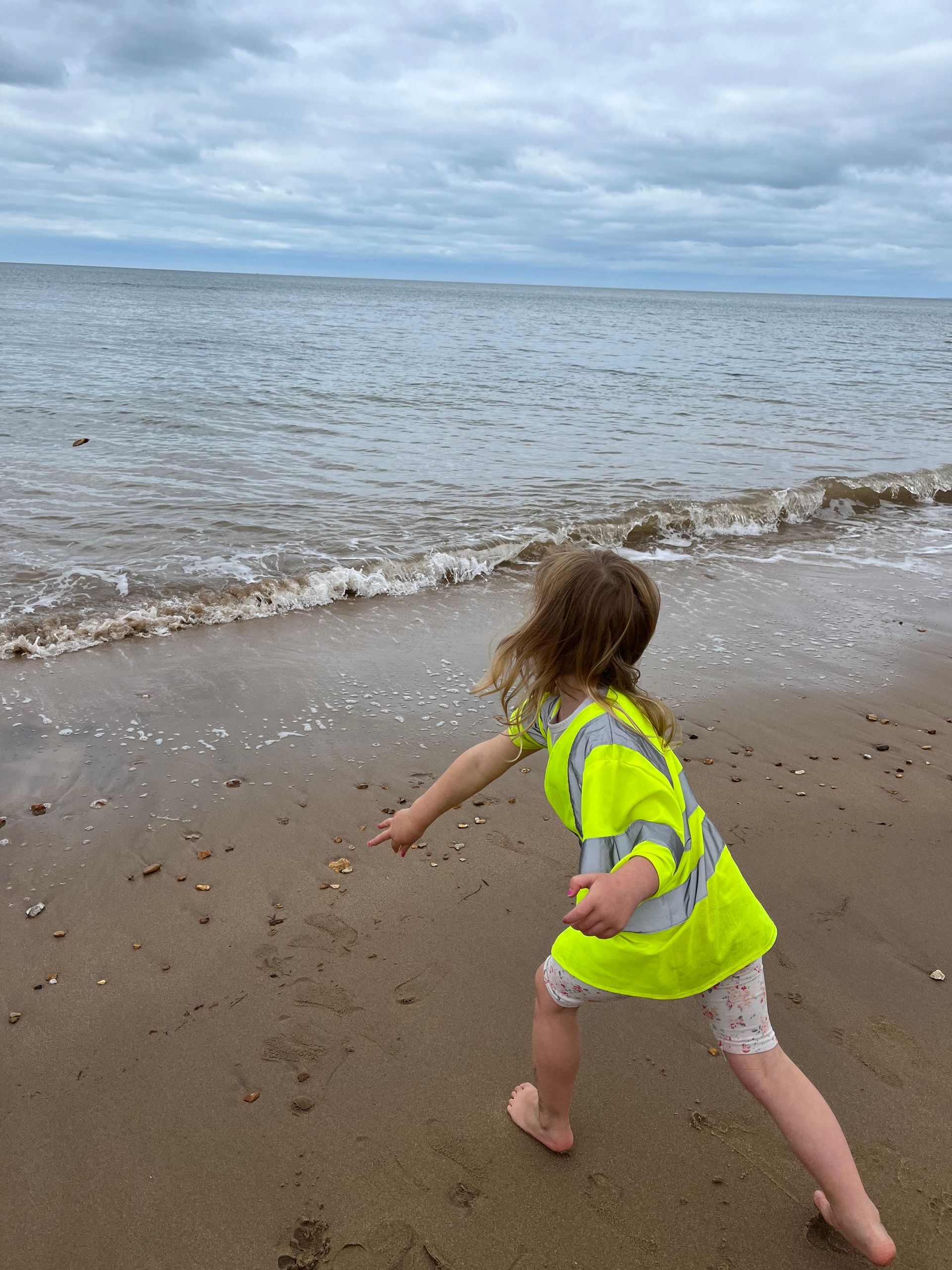 A little girl in a yellow vest is running on the beach