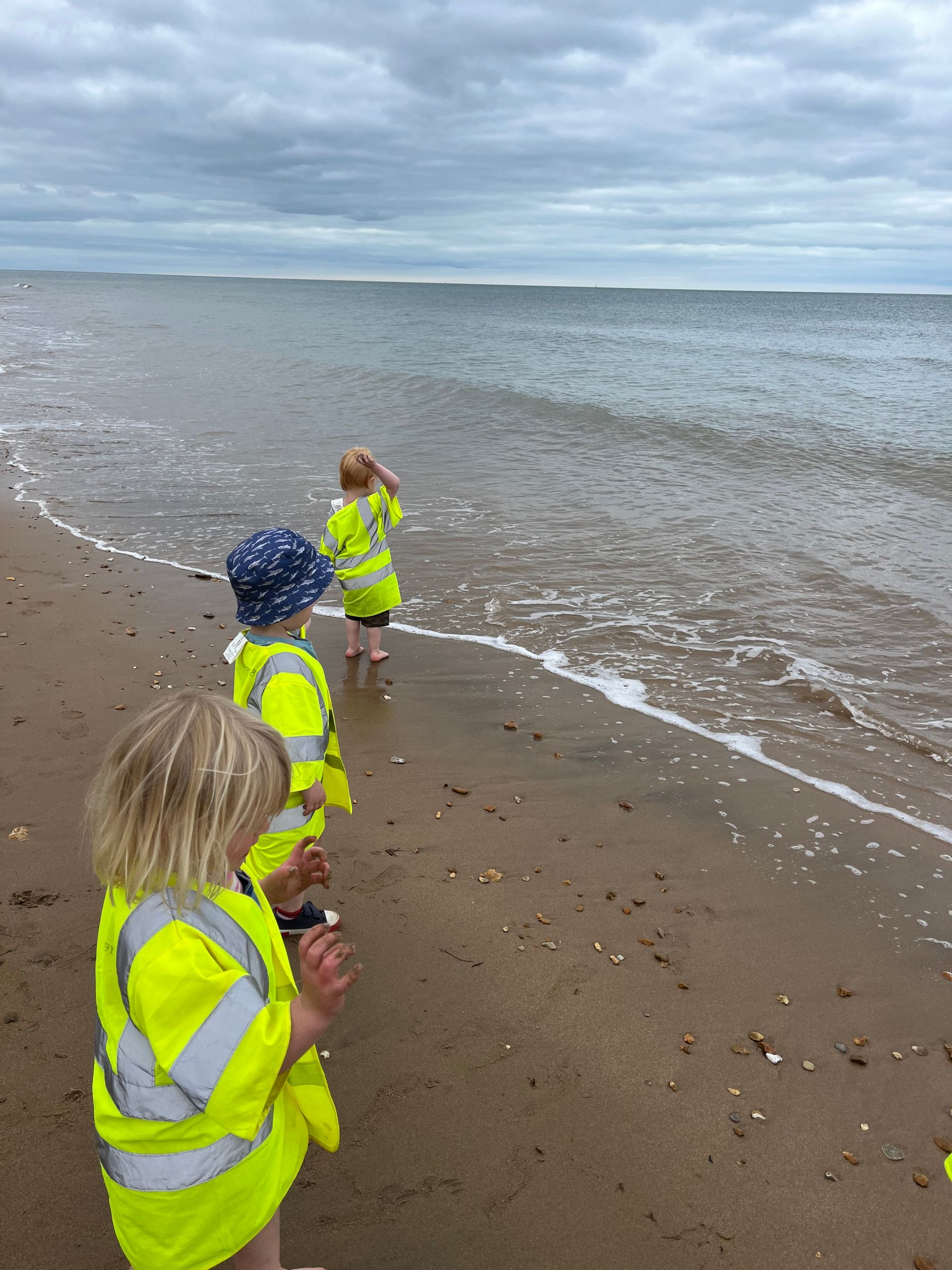 Two children are standing on a beach looking at the ocean.