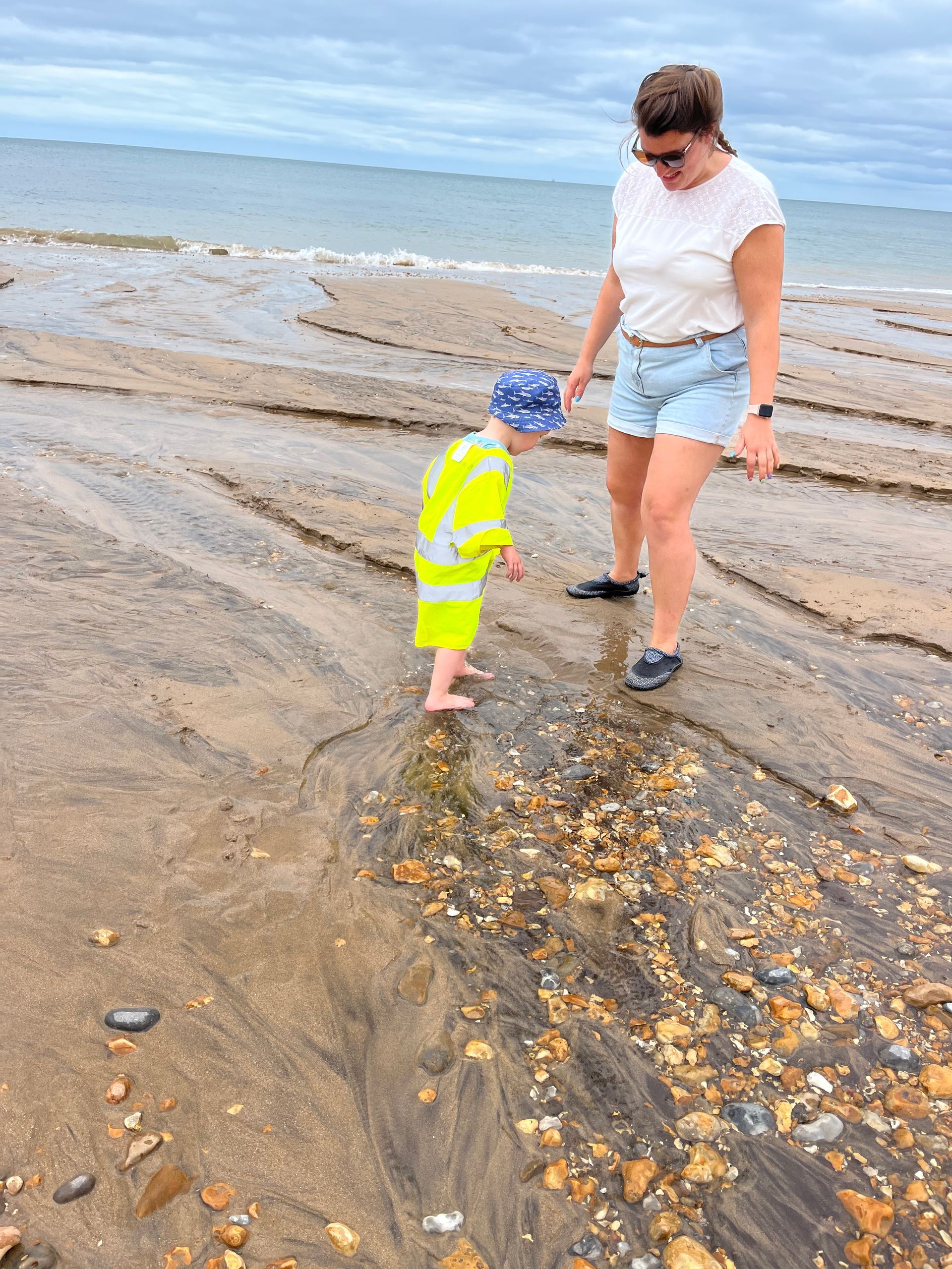 A woman and a child are standing on a beach near the water.