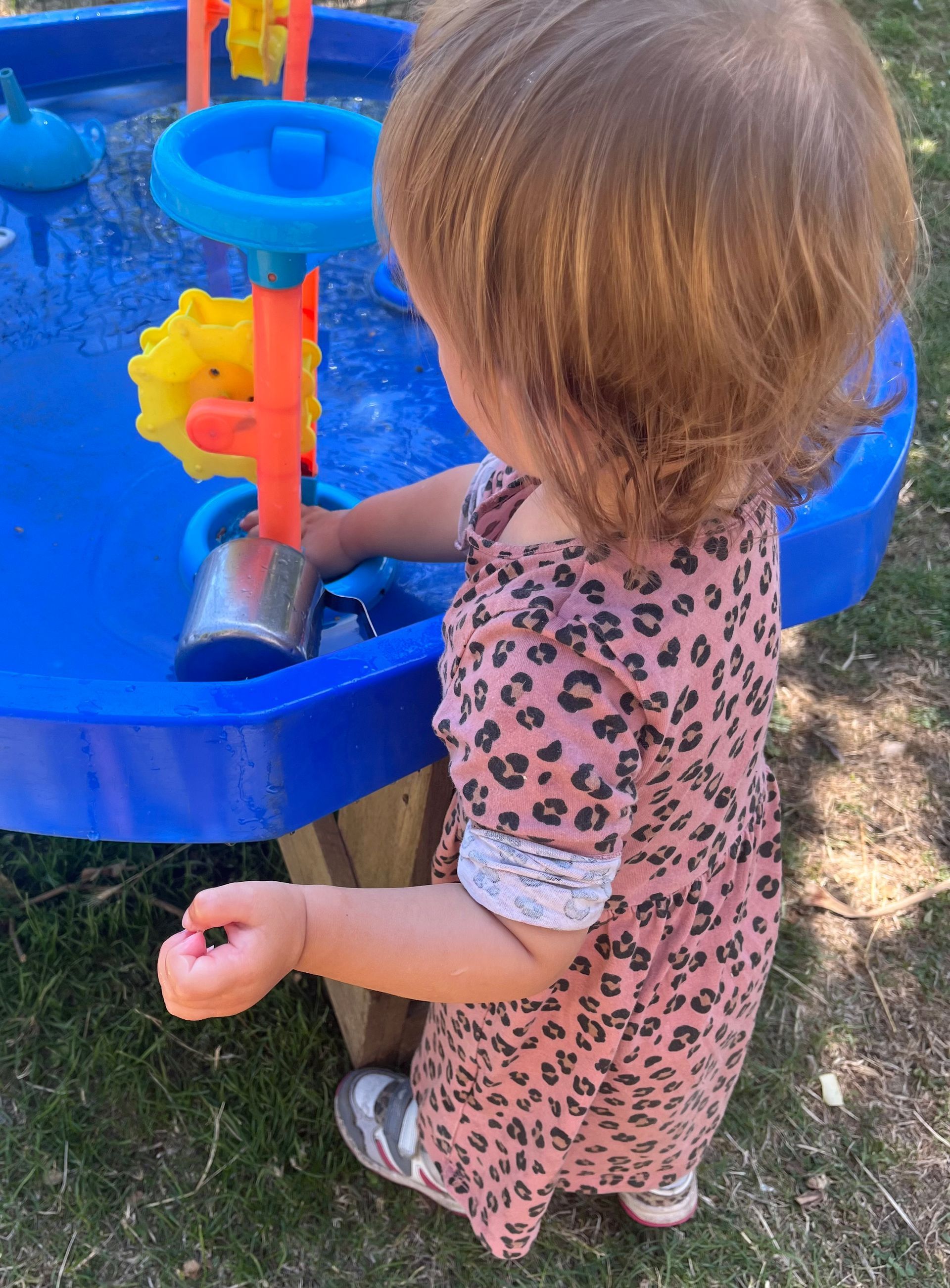 A little girl in a leopard print dress is playing with a water table.