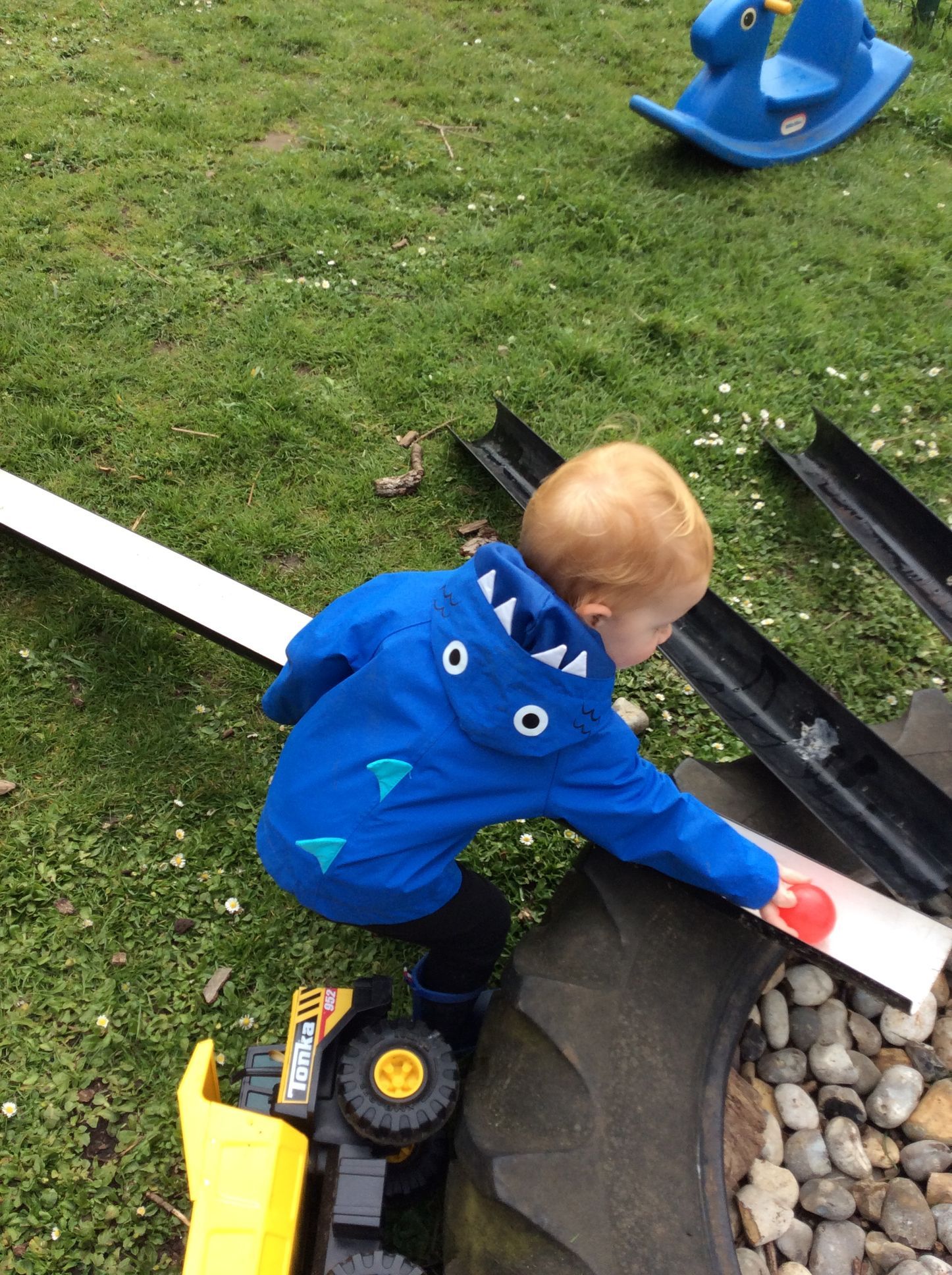 A little boy in a blue jacket is playing with a toy truck.