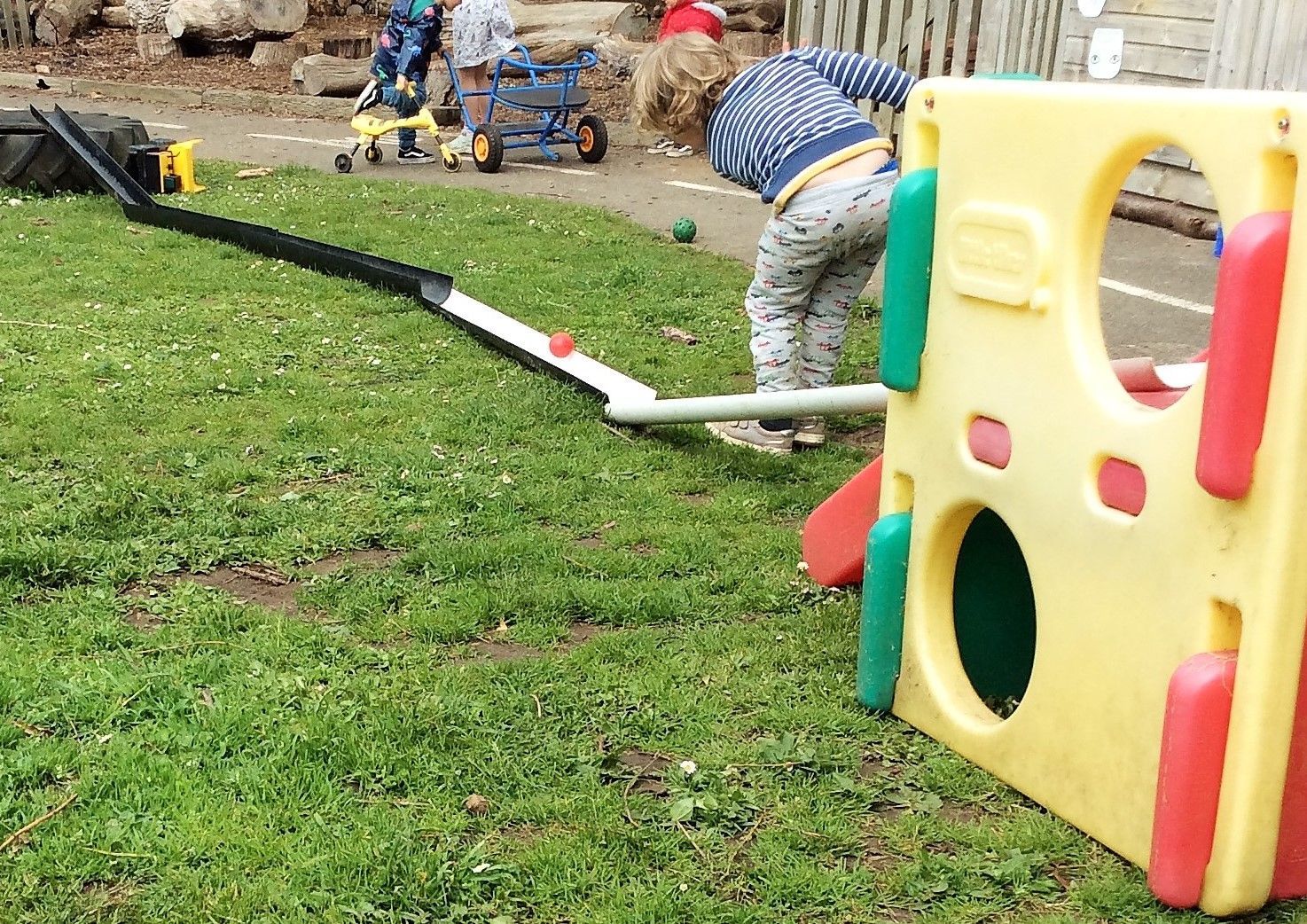 A child is playing with a toy slide in the grass.