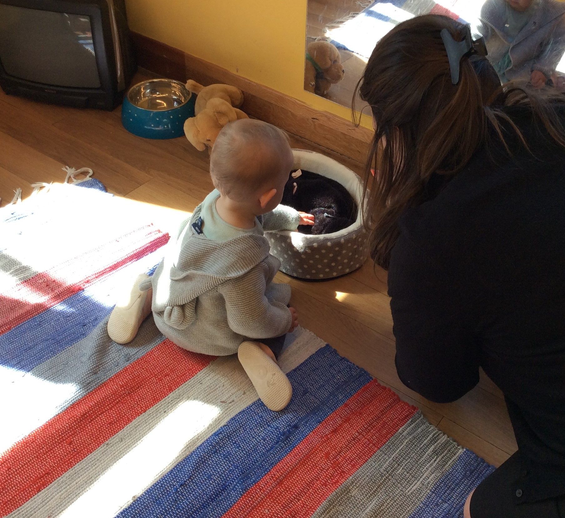 A woman kneeling down next to a baby on a rug
