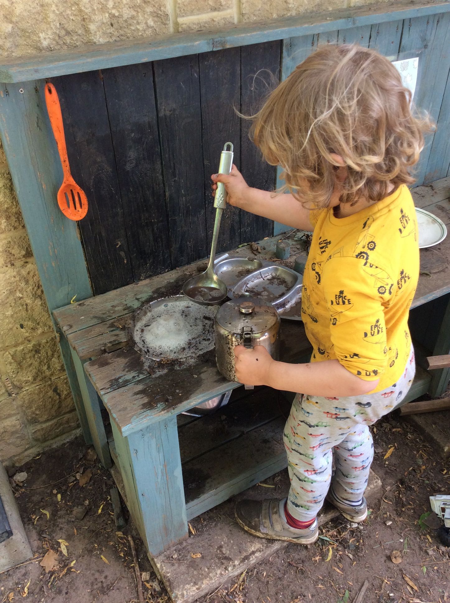 A little girl is playing in a mud kitchen.