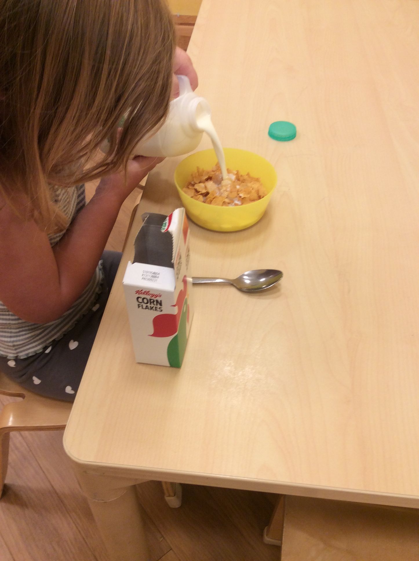 A little girl is pouring milk into a bowl of cereal.