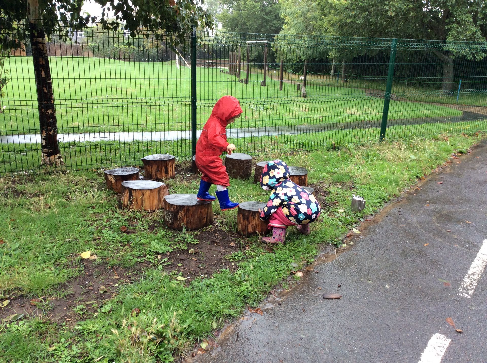 Two children are playing on tree stumps in the rain.