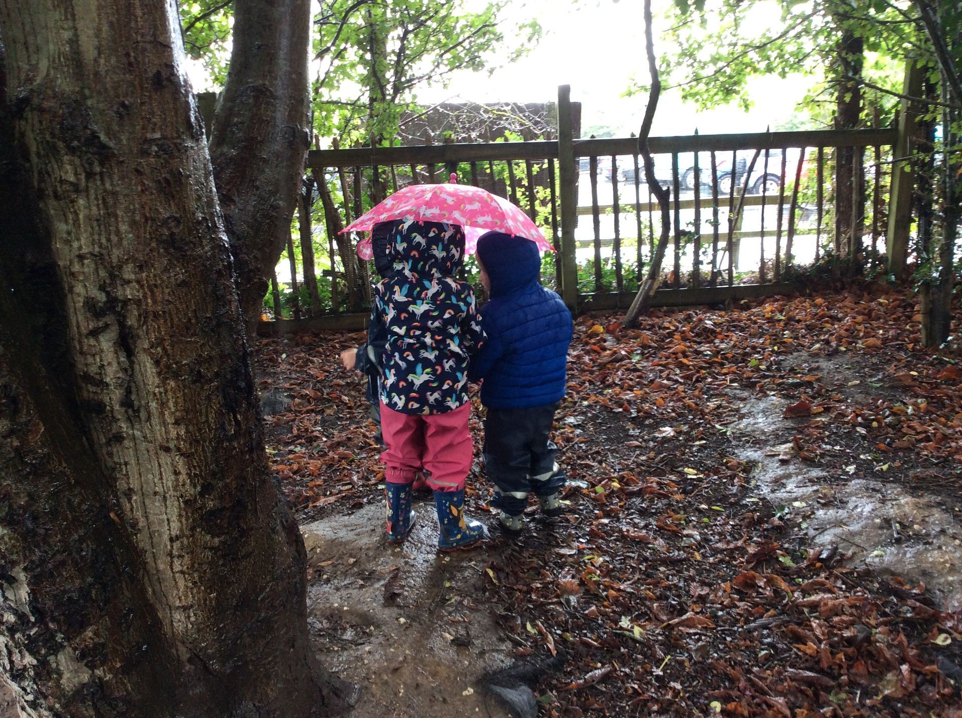 Two children are standing under an umbrella in the rain.