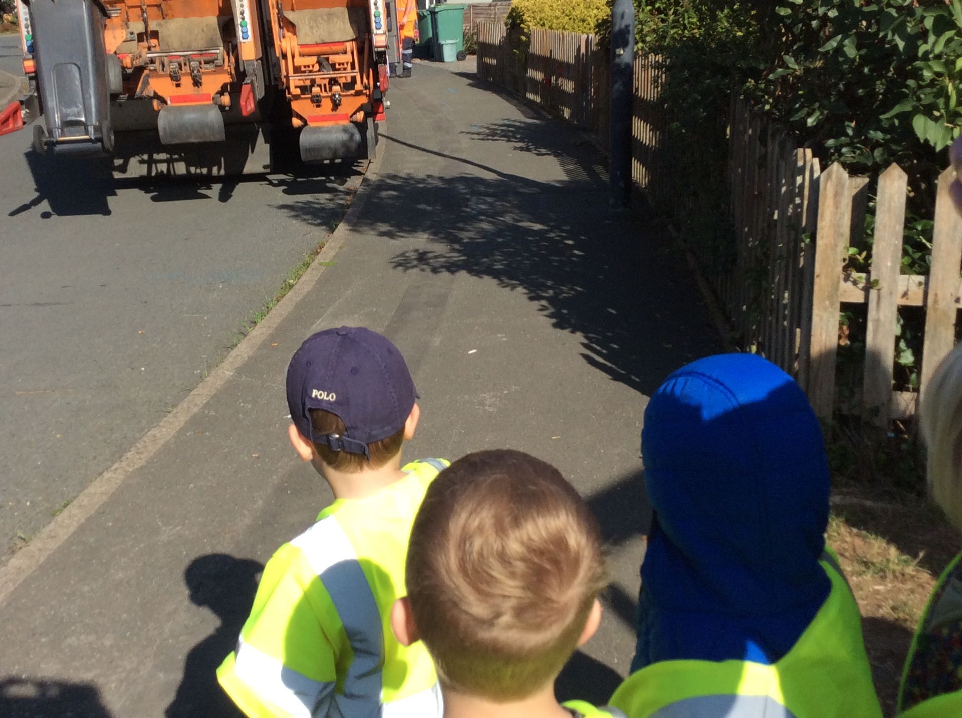 A group of children in yellow vests are walking down a street