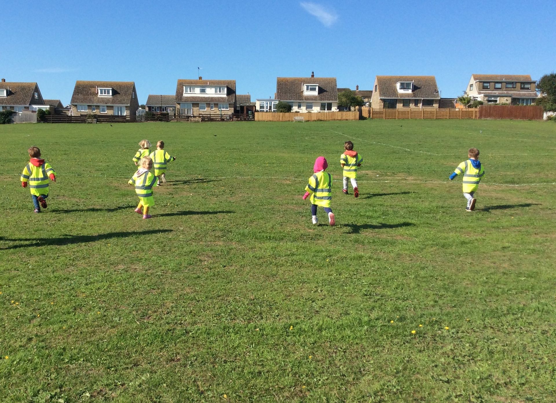 A group of children are running in a field with houses in the background