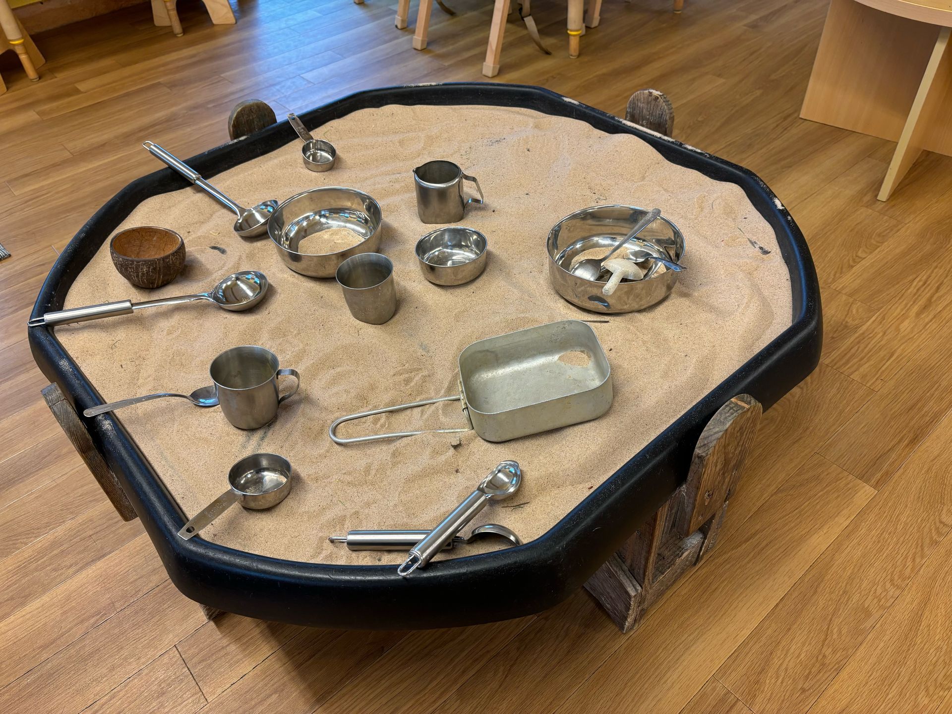 A sand table with stainless steel measuring cups and spoons on it.