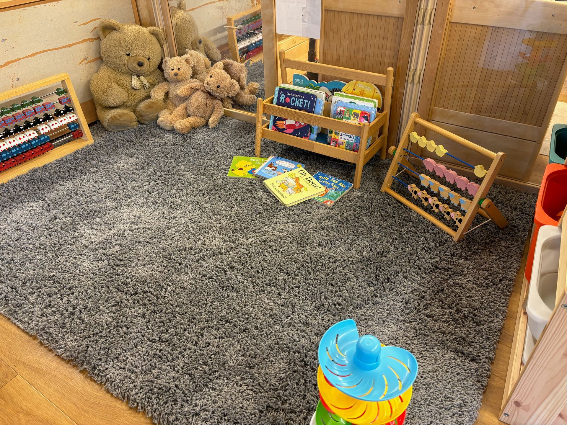 A room with teddy bears , books , and toys on the floor.