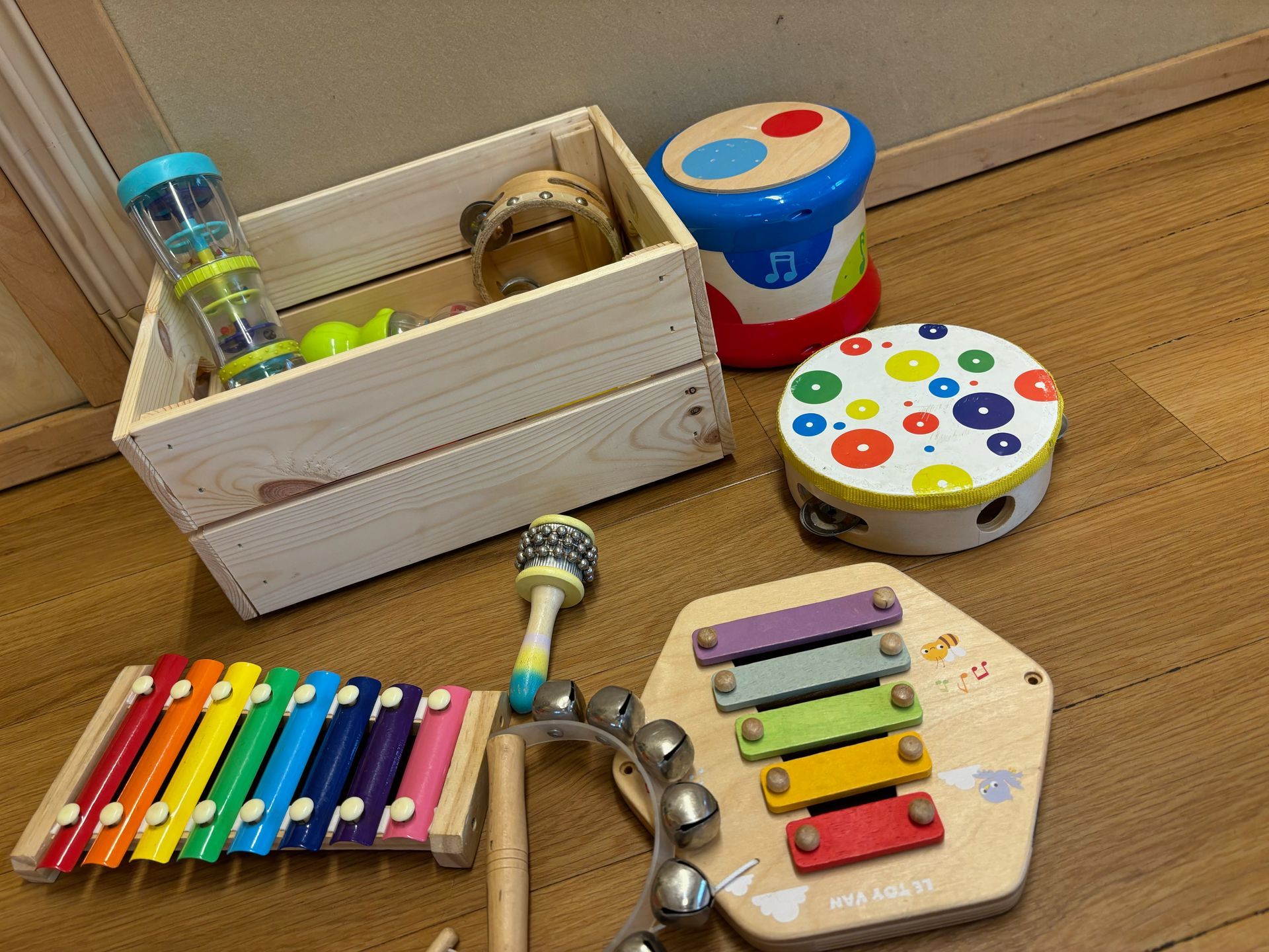 A wooden box filled with toys and a xylophone on a wooden floor.
