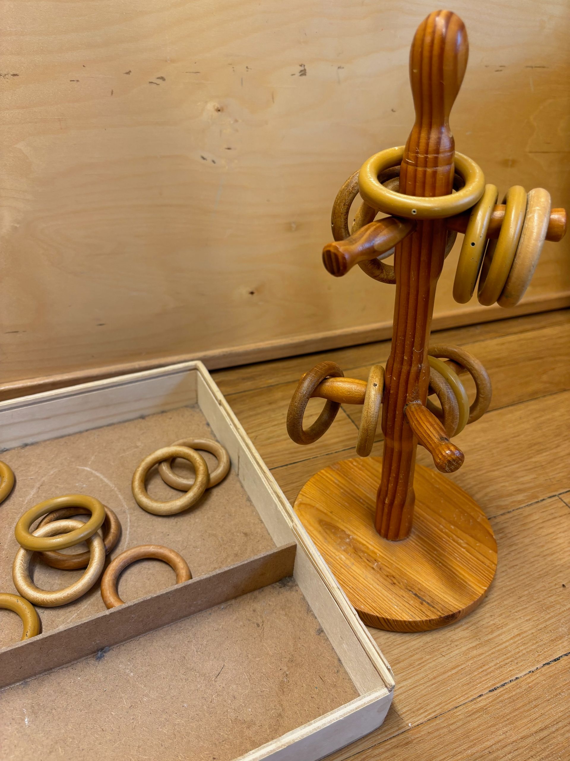 A wooden ring toss game is sitting on a wooden table next to a tray of rings.
