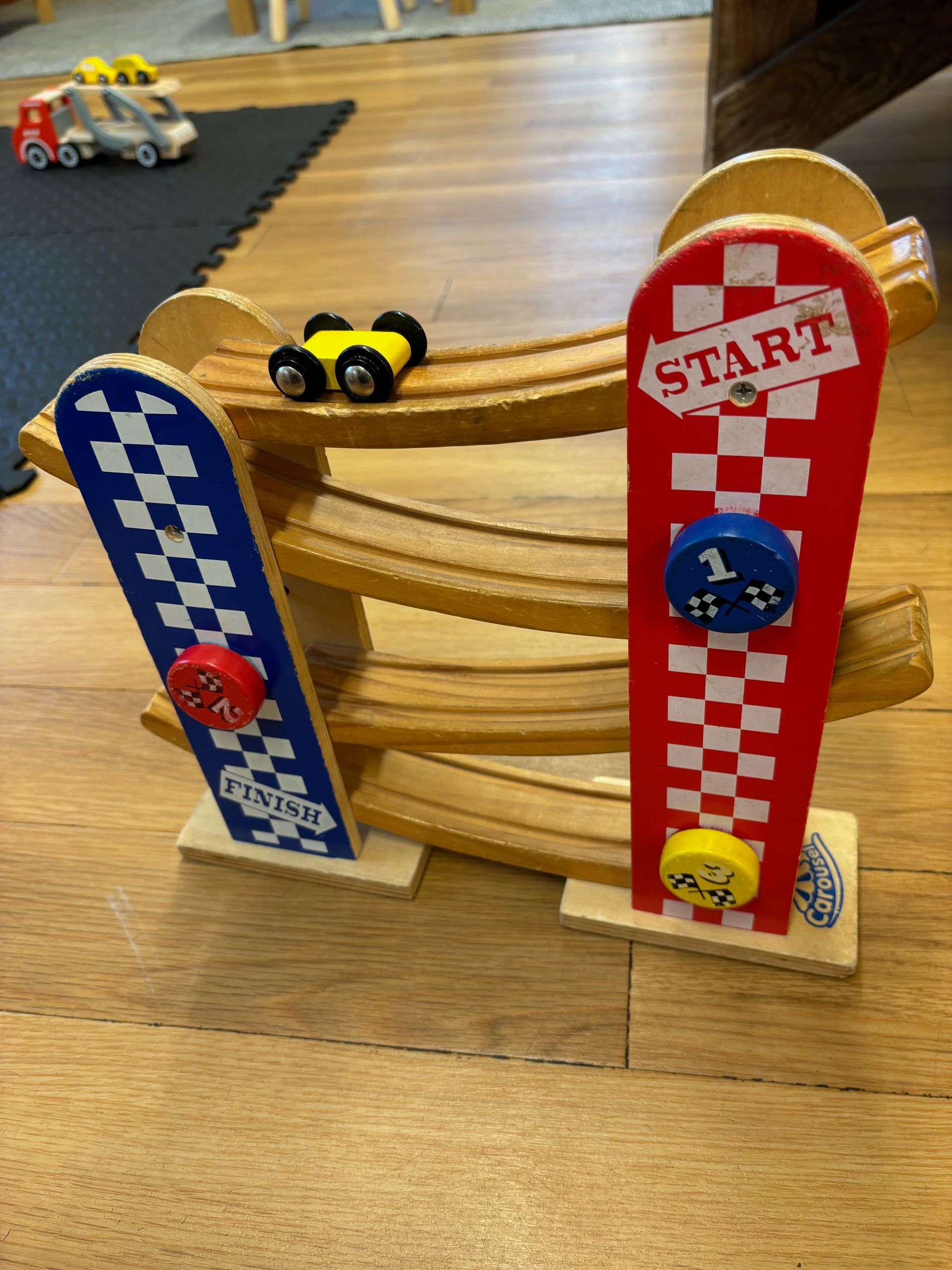 A wooden toy race track with two cars on it