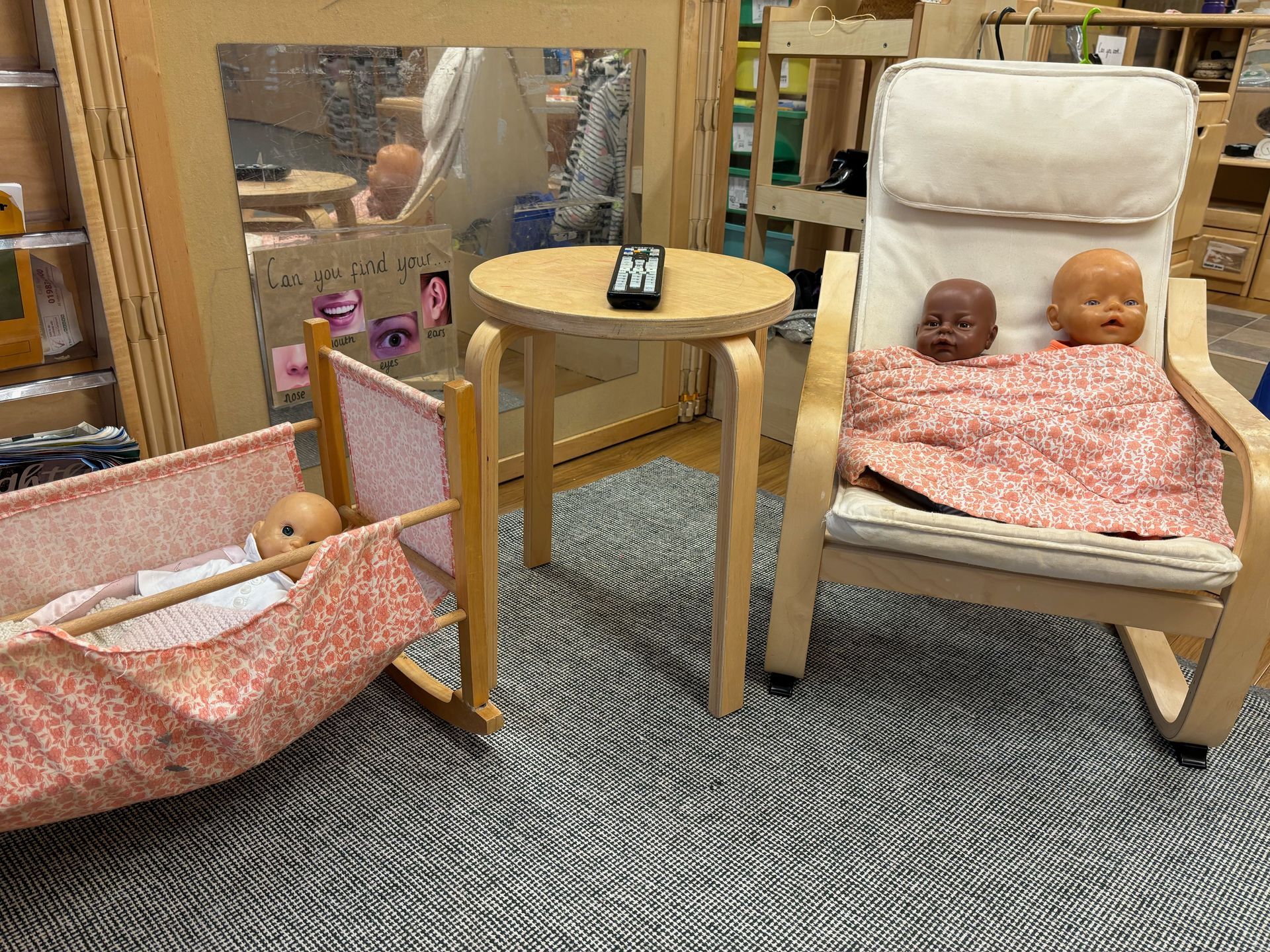 A room with two chairs , a table , a crib and two dolls.