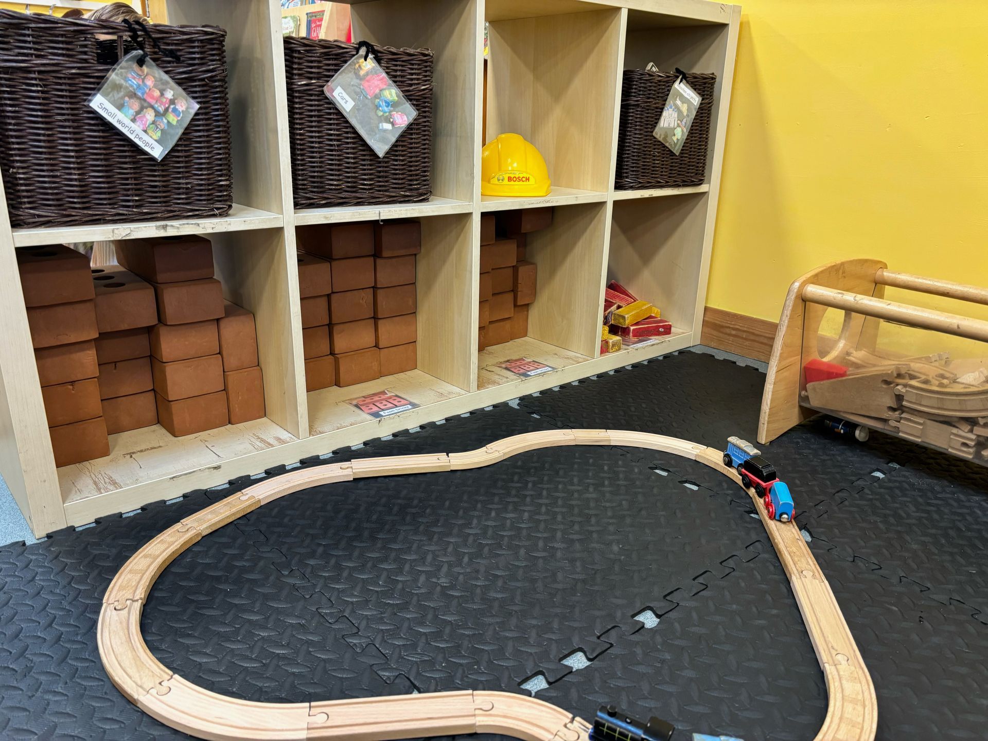 A wooden train track is sitting on the floor in a room.
