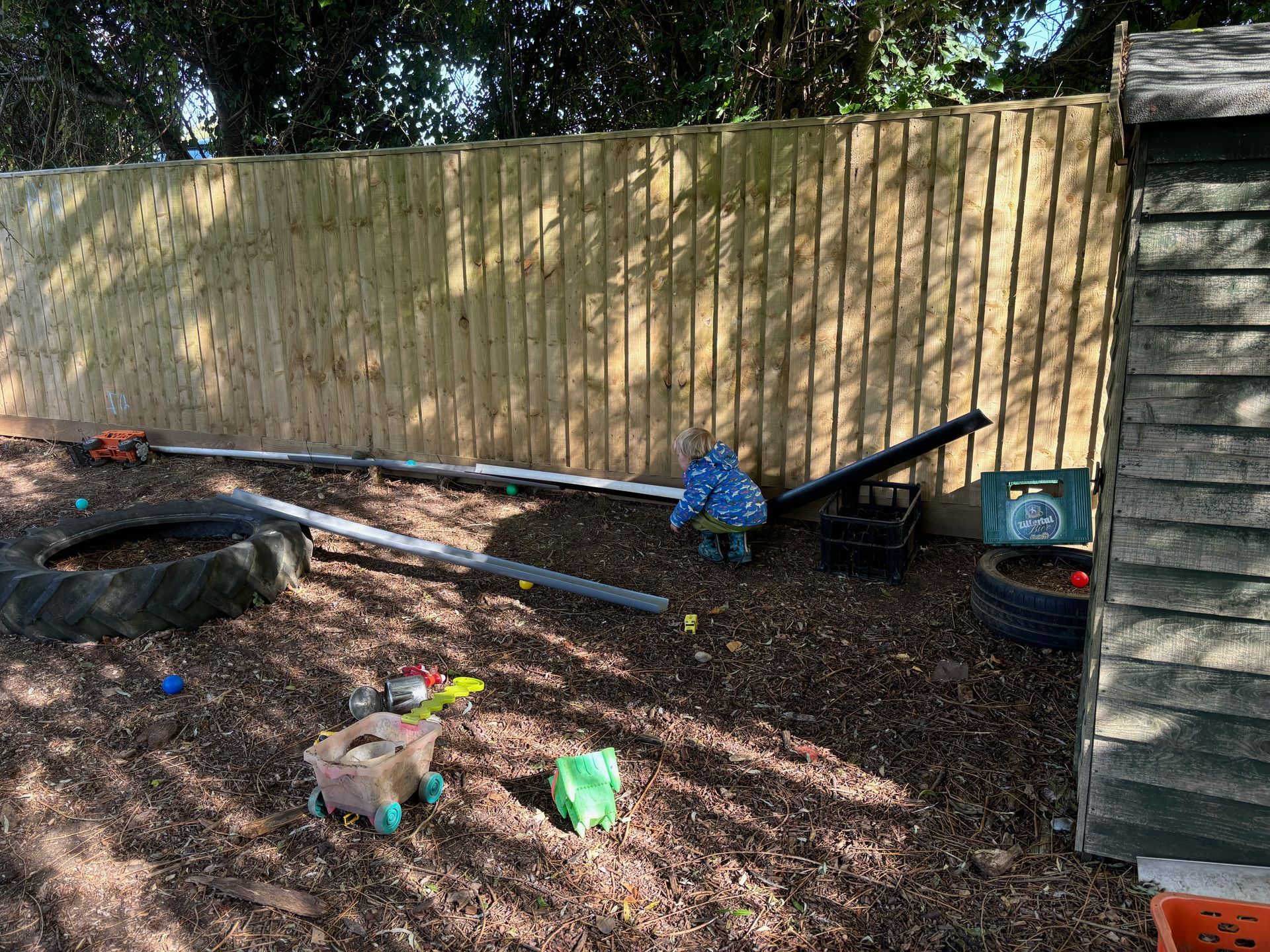 A wooden fence surrounds a sandbox filled with toys.