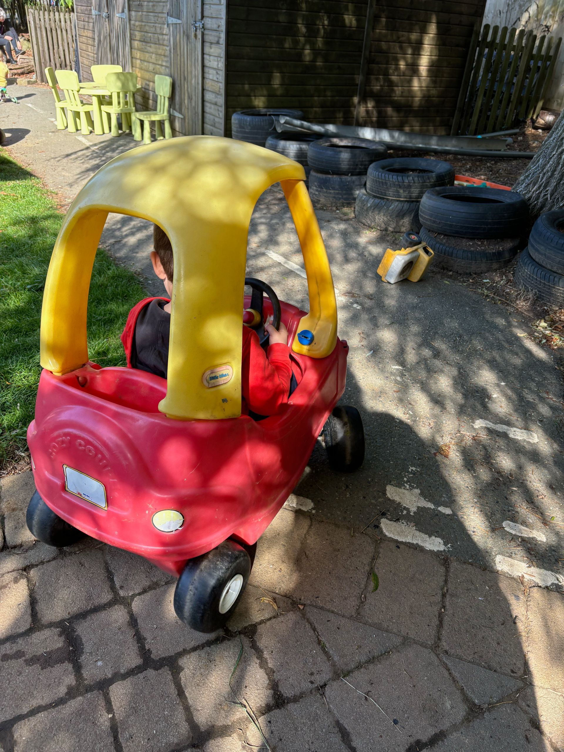A child is sitting in a red and yellow toy car.