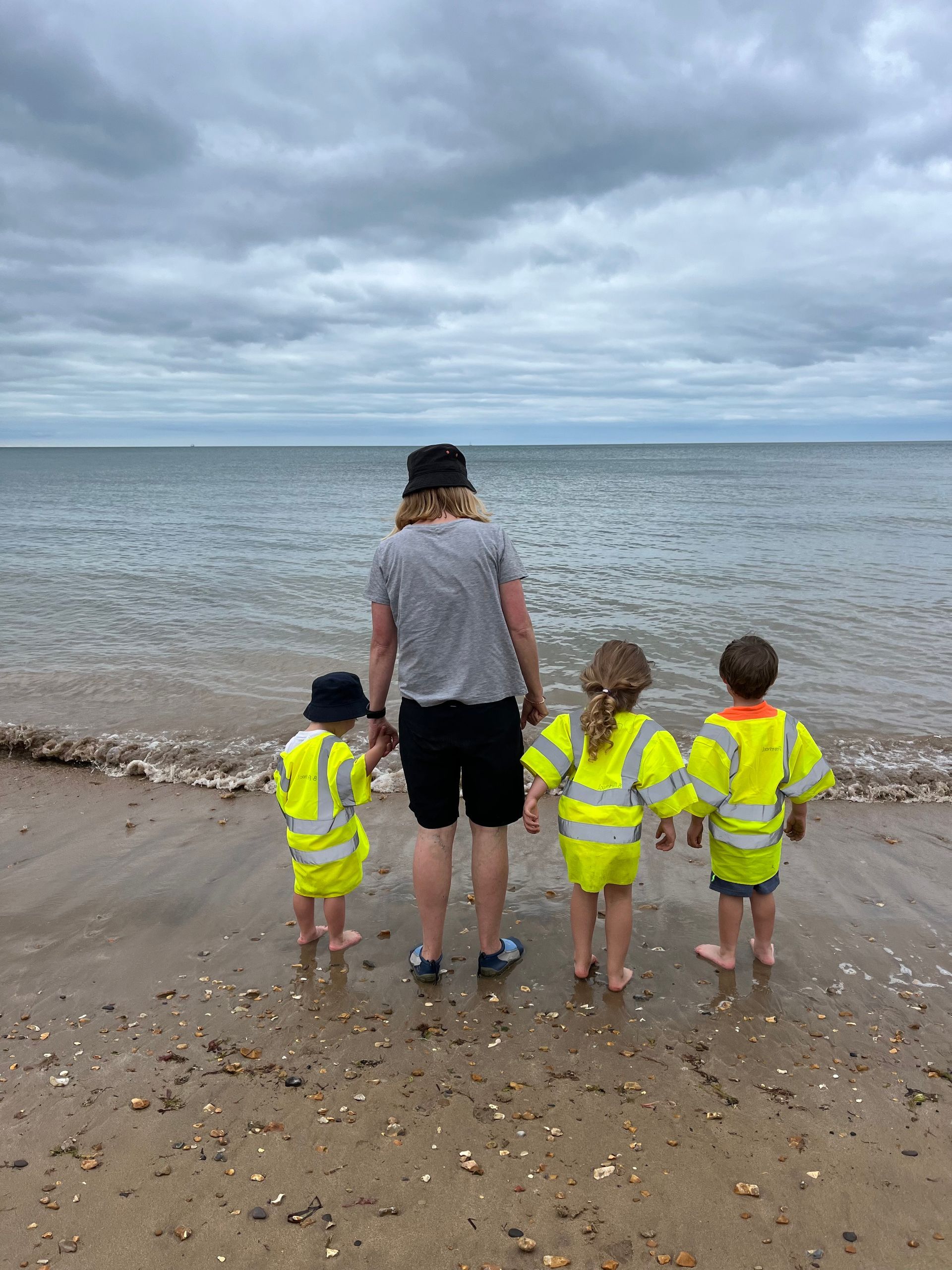 A woman and three children are standing on a beach looking at the ocean.