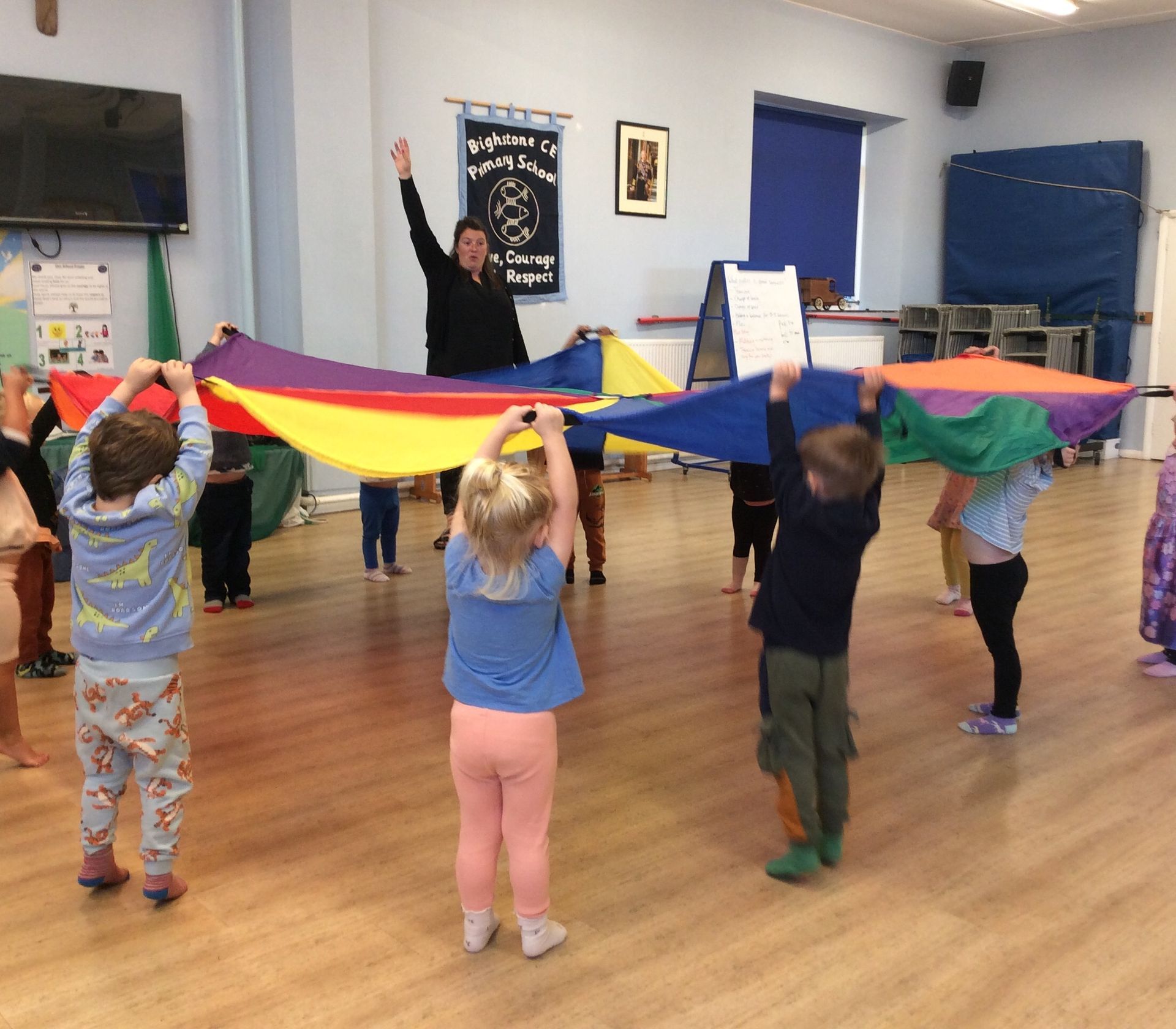 A group of children are holding colorful parachutes in a room