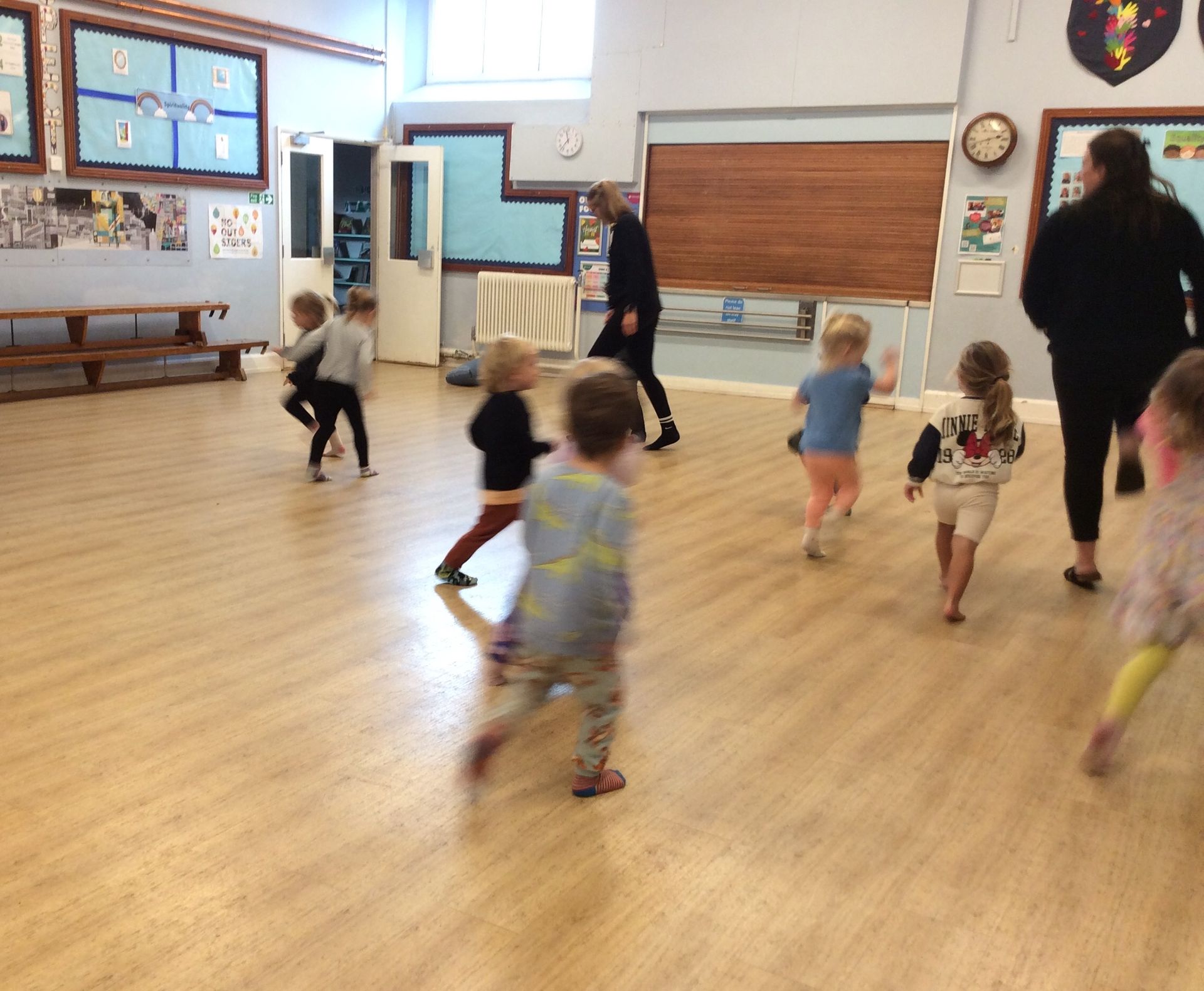 A group of children are running on a wooden floor in a room.
