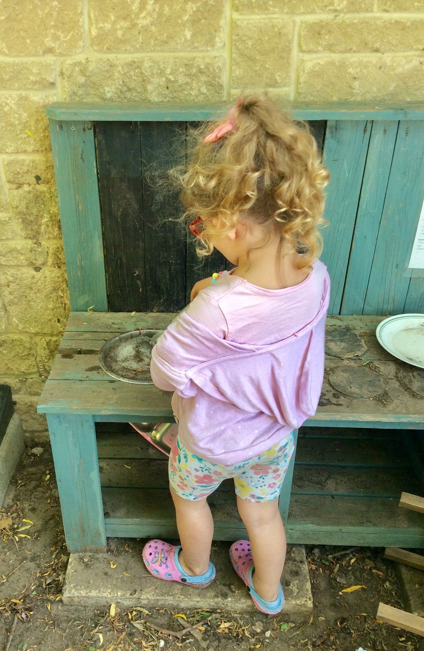 A little girl is standing next to a wooden bench.