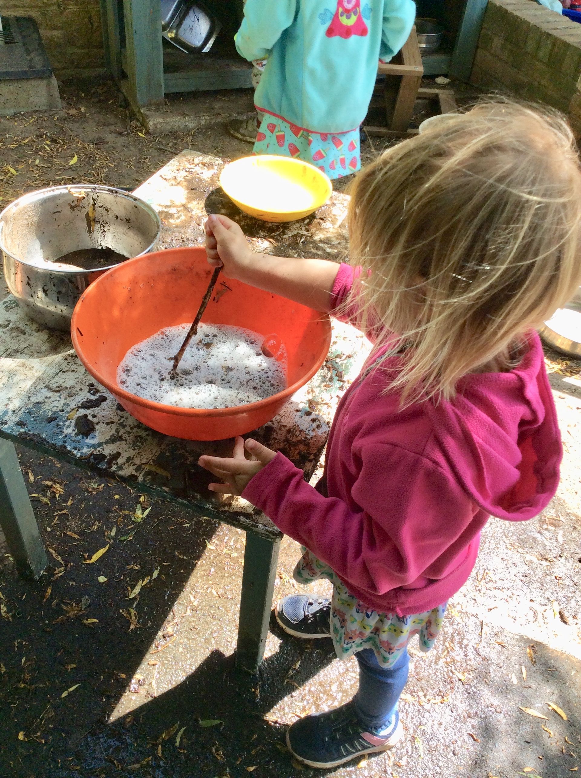 A little girl is mixing something in a bowl on a table.