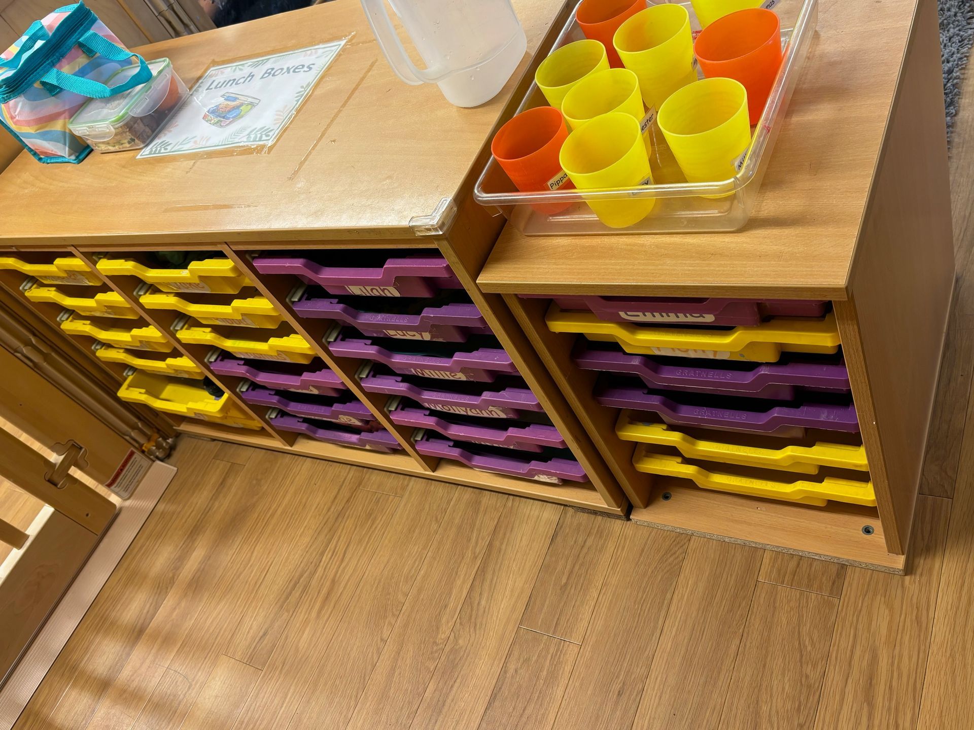 A wooden shelf with purple and yellow drawers and a tray of yellow cups.