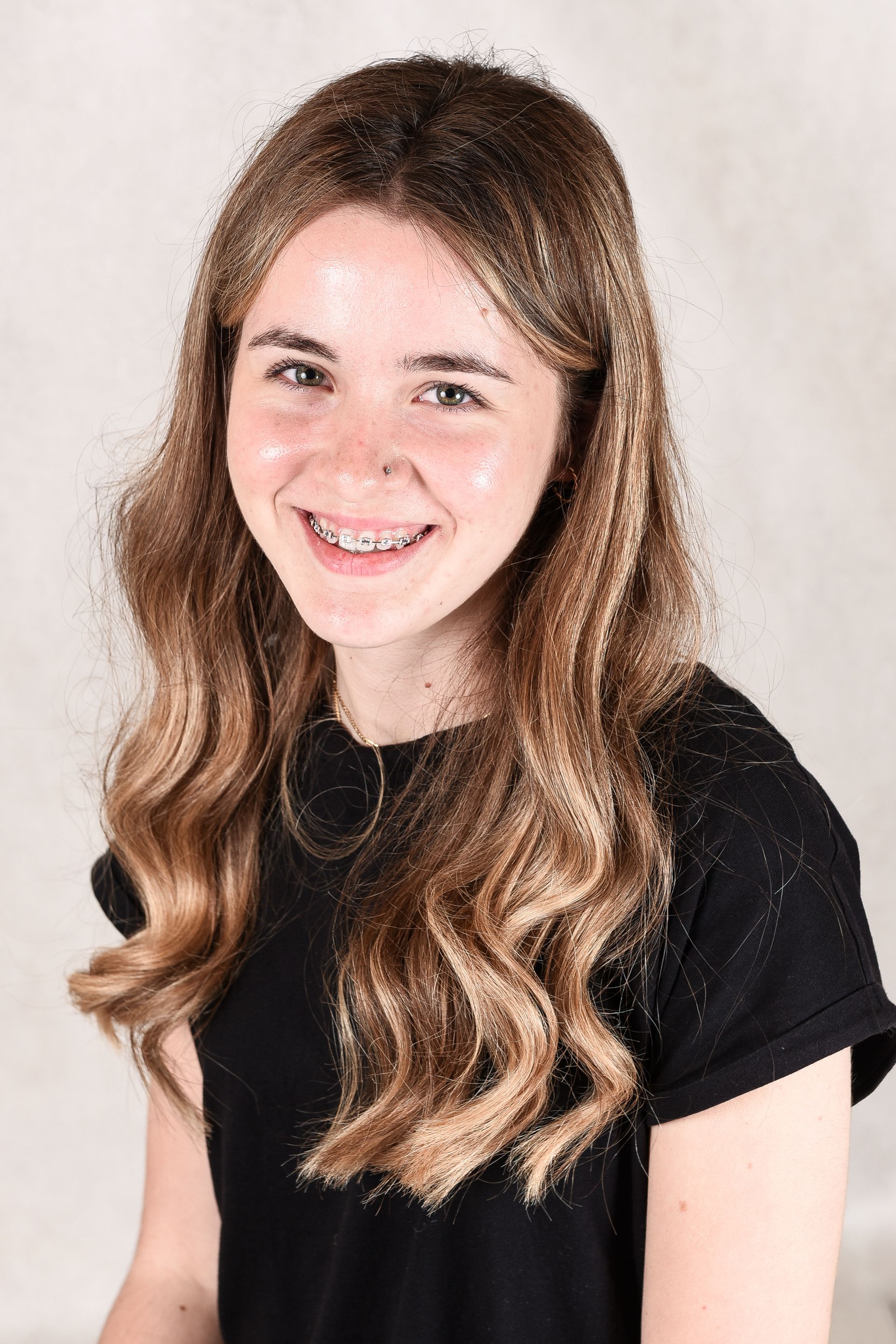 A woman wearing glasses and a white shirt is standing in front of a white wall.