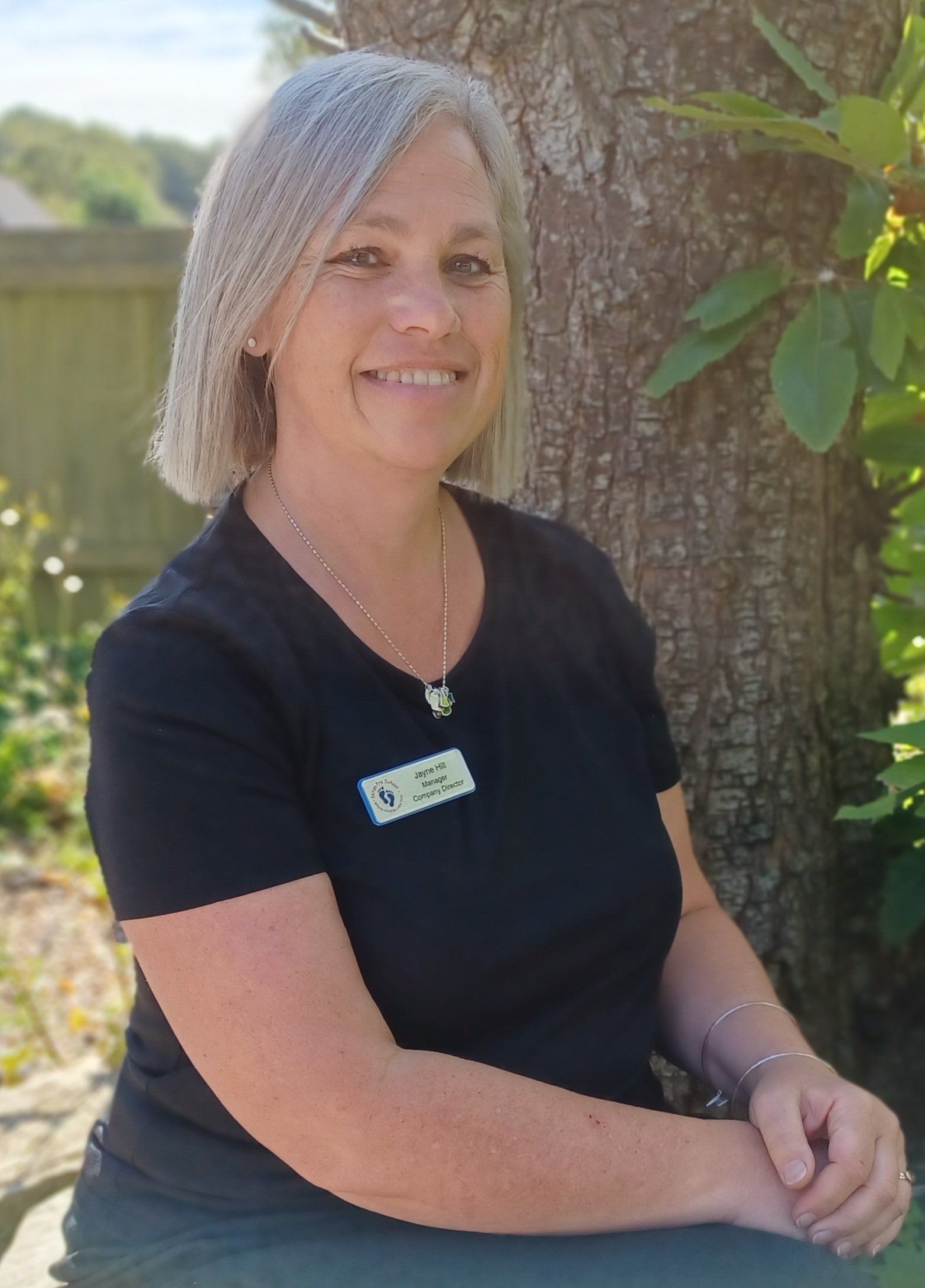 A woman in a black shirt is sitting next to a tree.