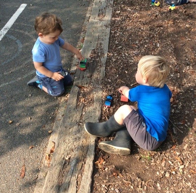 Two young boys are playing with toy cars on the side of the road