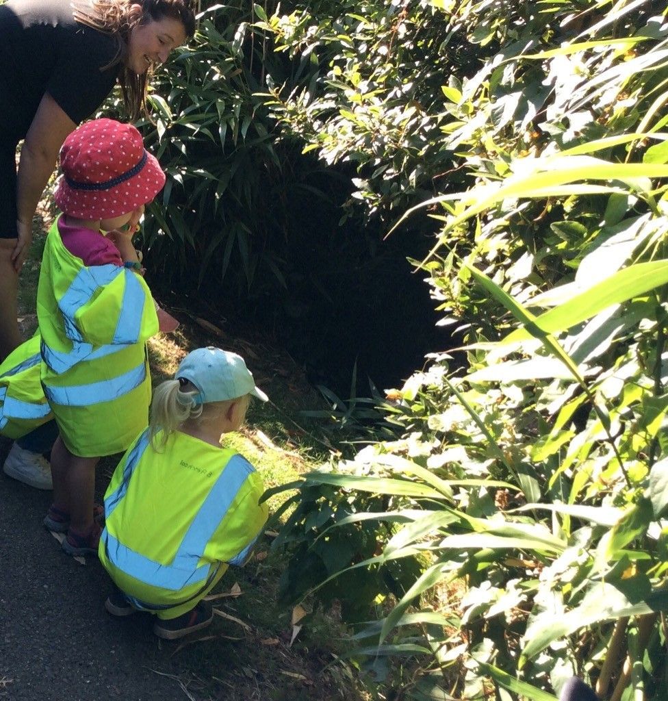 A woman and two children are looking into a hole in the ground.