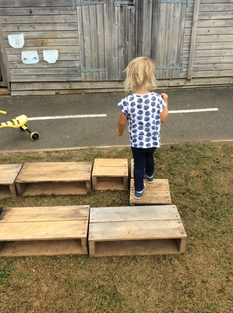 A little girl is standing on wooden blocks in front of a wooden building.