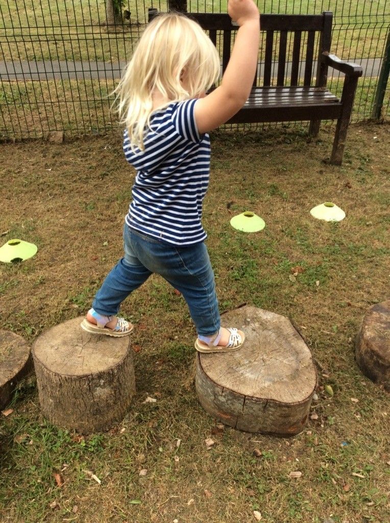 A little girl is standing on a log in a park.