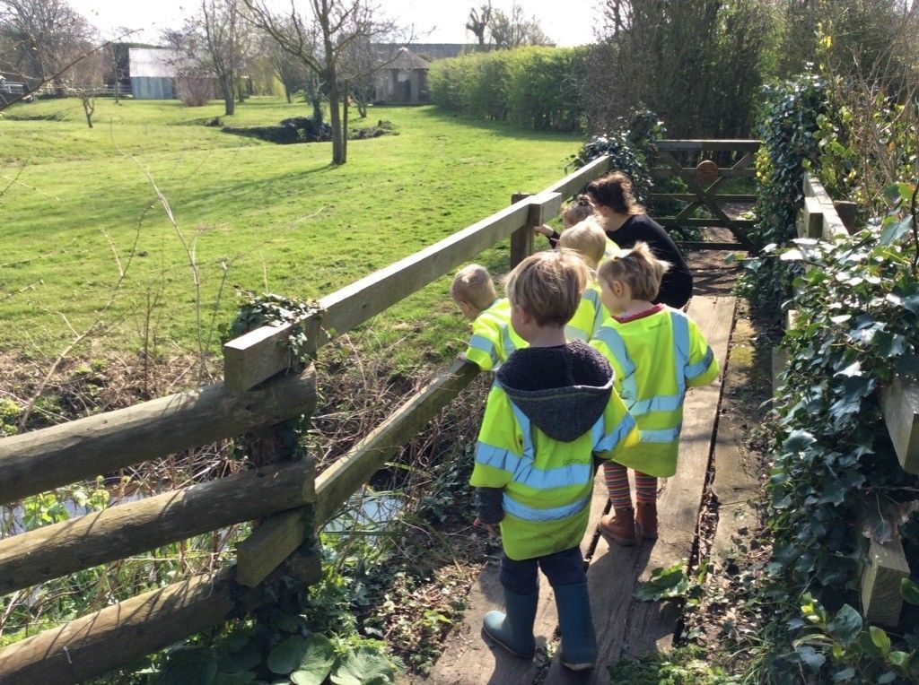 A group of children are walking across a wooden bridge in a field.