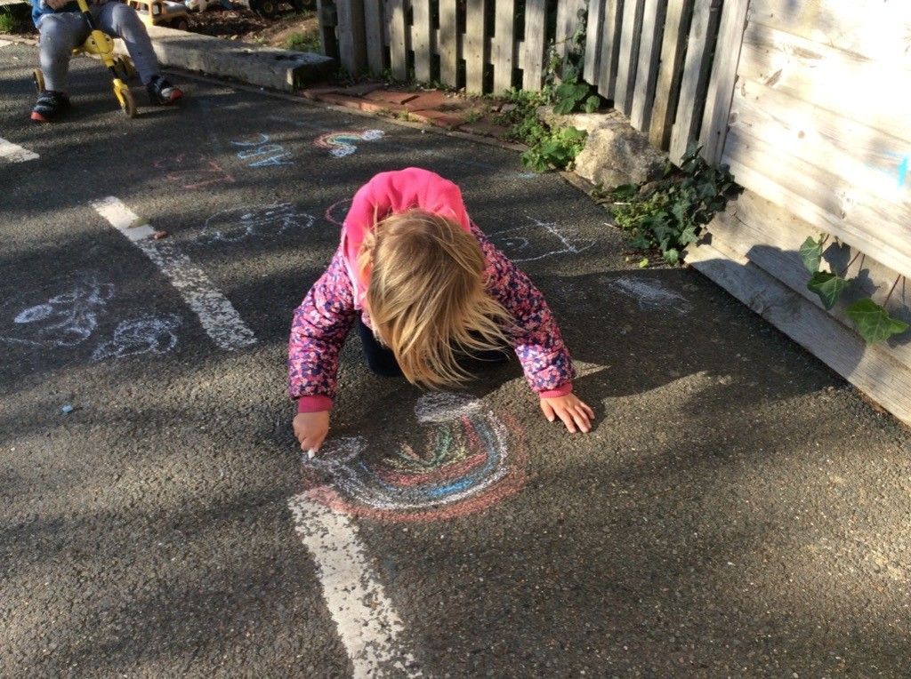 A little girl is drawing with chalk on the ground.