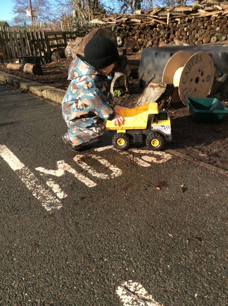 A little boy is playing with a toy truck on the side of the road.