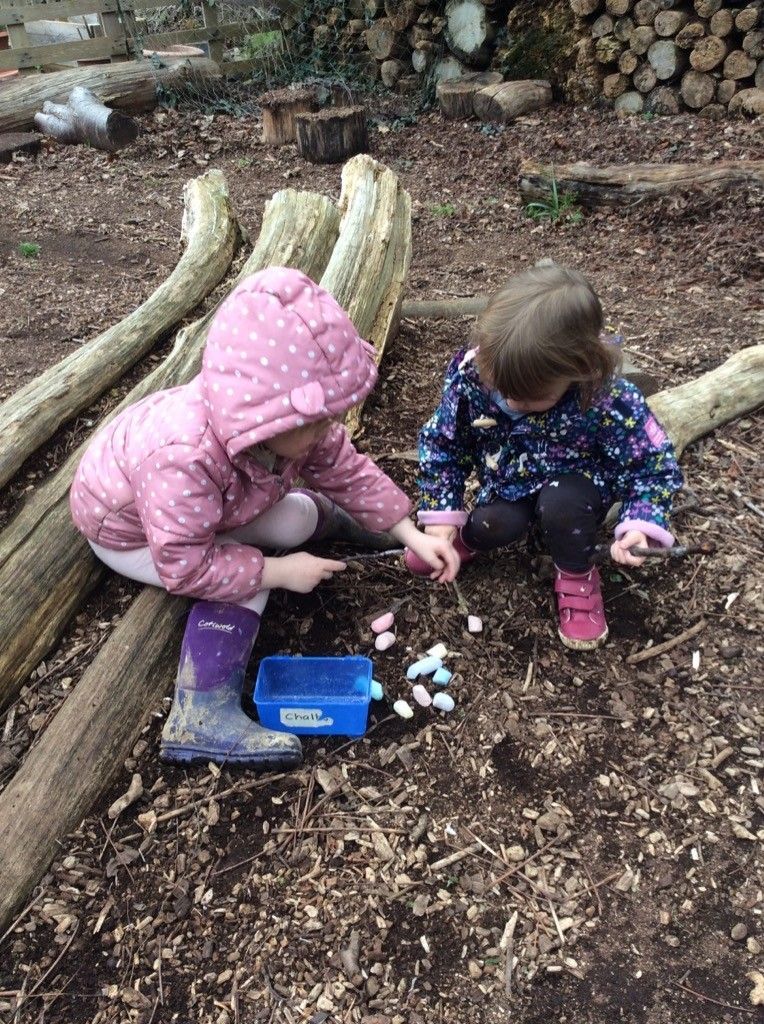 Two little girls are playing with chalk in the dirt.
