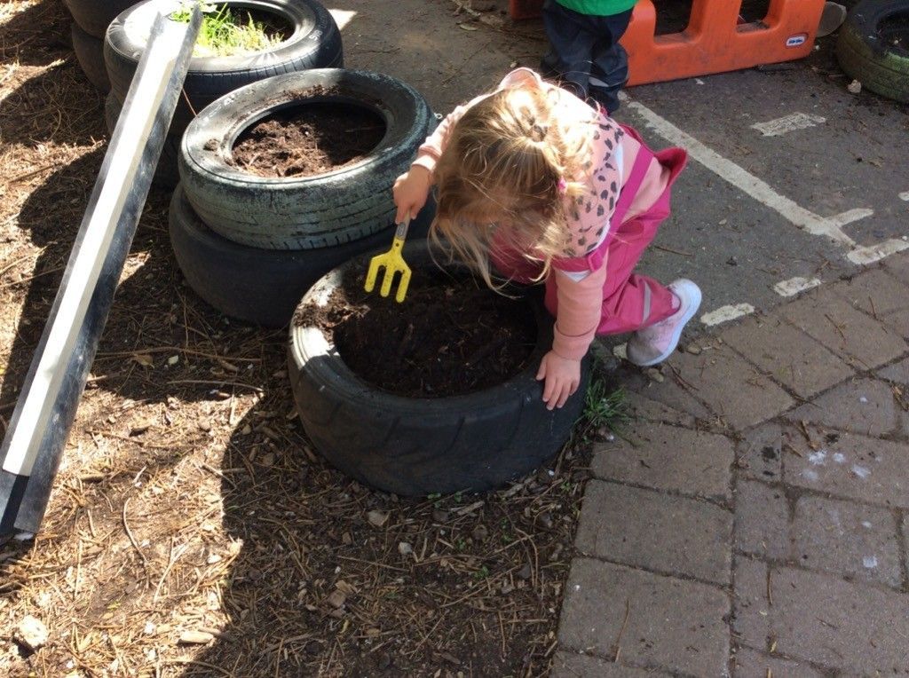 A little girl is playing with a yellow fork in a tire planter.