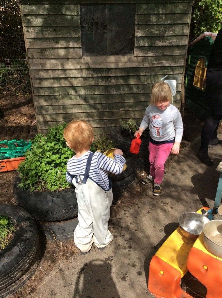 Two children are playing in the dirt in front of a wooden shed.